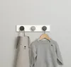A coat rack with three LEGO-style hooks on a light gray wall. A child's apron and sweater are hanging on the hooks. Anteprima dell’immagine prodotto