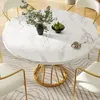 A round marble dining table with gold legs, surrounded by white chairs, set in a dining room. Produktbild-Vorschau