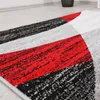 A close-up view of a geometric patterned rug with red, gray, white, and black colors. Voir les images du produit