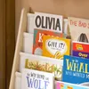 A close-up view of a wooden tiered bookshelf filled with children's books. Produktbild-Vorschau