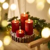 Four red LED candles of varying heights are arranged on a wooden base, surrounded by pine branches and fairy lights, creating a festive and warm atmosphere. Produktbild-Vorschau