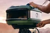 A person is adjusting a portable pizza oven outdoors. Produktbild-Vorschau