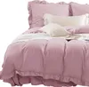A close-up view of a pink bedding set with ruffled edges, featuring several pillows and a white knitted throw blanket. Podgląd zdjęcia produktu