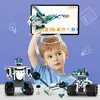 A young boy is holding a robot model in front of a tablet screen displaying a coding interface, with other robot models and building blocks around him. Náhled obrázku produktu
