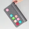 A hand is shown unrolling a silicone macaron mat with colorful macarons on it. Podgląd zdjęcia produktu