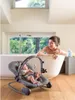 A woman is taking a bath while a baby is in a bouncer next to the tub. Produktbild-Vorschau