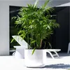 A white planter with a green plant sits on a white patio next to a white lounge chair. Náhled obrázku produktu