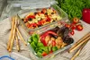 Two glass food containers filled with salads and pasta salad, along with breadsticks and fresh vegetables, are arranged on a checkered cloth. Produktbild-Vorschau