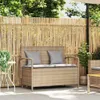 A beige poly rattan garden bench with storage and gray cushions is placed on a patio in front of a bamboo fence, with plants and trees in the background. Náhľad obrázku produktu