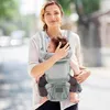 A woman is holding a baby in a baby carrier while walking outdoors. Náhled obrázku produktu