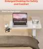 A laptop, headphones, and mouse are placed on a white table that is positioned over a bed. A cup holder with a cup is attached to the side of the table. Produktbild-Vorschau