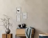 A styled vignette featuring framed pictures on a wall, a wooden cabinet with a teapot and mug, and a vase with branches. Produktbild-Vorschau