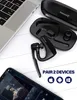 A black Bluetooth headset and its charging case are displayed on a white surface next to a laptop and a smartphone. Produktbild-Vorschau
