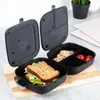 An open black lunchbox with a sandwich in one compartment and cookies and tomatoes in another, placed on a wooden cutting board. Náhľad obrázku produktu