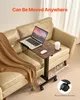 A portable laptop table with wheels is placed next to a sofa, with a laptop, mouse, glasses, and a drink on it. Náhled obrázku produktu