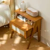 A wooden nightstand with items on it, next to a bed. Náhled obrázku produktu