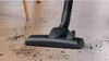 A vacuum cleaner head cleaning a wooden floor with scattered dirt. Produktbild-Vorschau
