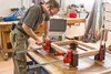 A carpenter is using a frame clamp set to assemble a wooden frame in a workshop. Produktbild-Vorschau