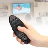 A hand holding a black TV remote in front of a blurred background showing a TV and living room. Anteprima dell’immagine prodotto