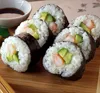 A close-up view of several sushi rolls filled with shrimp and avocado, arranged on a wooden surface with a small dish of soy sauce in the background. Produktbild-Vorschau