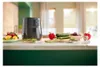 A black air fryer is displayed on a kitchen counter with various fresh vegetables and fruits arranged around it. Produktbild-Vorschau