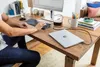 A person's hands are visible typing on a keyboard at a wooden desk, with a laptop and monitor set up. Produktbild-Vorschau