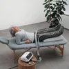 An elderly woman is lying on a massage table with her legs elevated and wrapped in a compression device. Produktbild-Vorschau
