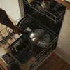 A person is loading pans into a dishwasher. Podgląd zdjęcia produktu