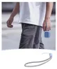 A person walking outdoors, holding a small blue device attached to their wrist with a gray strap. Anteprima dell’immagine prodotto