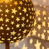 A close-up of a solar-powered decorative sphere with star cutouts, casting star-shaped shadows on a textured wall. Produktbild-Vorschau