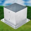 A galvanized metal post base with a square opening and a flat base with mounting holes, set against a blurred background of green grass and a blue sky. Náhled obrázku produktu