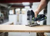 A person is using a jigsaw to cut a piece of wood in a workshop. Produktbild-Vorschau