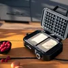 A waffle maker with batter is open on a wooden table, with a bowl of raspberries and eggs nearby. Voir les images du produit