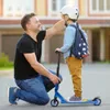 A father is helping his son put on his helmet before riding a scooter. Náhľad obrázku produktu