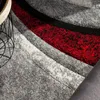 A close-up view of a textured rug with abstract geometric stripes in red, black, and gray. Produktbild-Vorschau