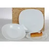 Three white plates of different sizes are arranged on a surface with a wooden board in the background. One plate has a piece of corn on it. Podgląd zdjęcia produktu