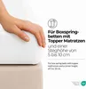 A hand is shown pressing down on a white fitted sheet that is placed over a beige mattress topper. Text overlays describe the product's suitability for box spring beds with topper mattresses. Produktbild-Vorschau