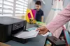 A person is loading paper into a printer while a child stands in the background. Podgląd zdjęcia produktu
