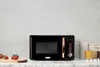 A retro-style black microwave with copper accents sits on a marble countertop, with strawberries on a wooden board to the left and canisters and a yellow mug to the right. Anteprima dell’immagine prodotto