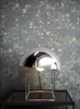 A modern chrome mushroom-shaped table lamp with a metallic gold and dark gray textured wallpaper background. Produktbild-Vorschau
