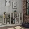 A modern white bookshelf filled with books and decorative items, placed against a textured wall and brick wall. A window is visible on the right side, and a rug is on the floor. Produktbild-Vorschau