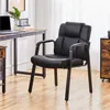 A black faux leather office chair is shown in a room with a desk and filing cabinet. Produktbild-Vorschau