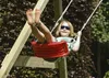 A child is swinging on a red swing set in a garden. Anteprima dell’immagine prodotto