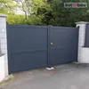A dark gray metal gate with a gold doorknob, set against a backdrop of trees and foliage. Produktbild-Vorschau
