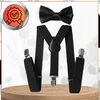 A black bow tie and suspender set is displayed on a wooden surface against a light, floral-patterned background. Produktbild-Vorschau