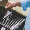 A person's hand is lifting the lid of a black gas grill. Anteprima dell’immagine prodotto
