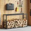 A black metal firewood rack filled with logs, set against a wood-paneled wall with various tools hanging. Podgląd zdjęcia produktu