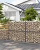 A gabion wall with a wooden fence section and a white sphere on top, in front of a white house with green trees. Produktbild-Vorschau