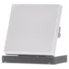 A white square switch cover is shown tilted on a dark gray base. Náhled obrázku produktu