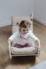 A young child sits in a wooden rocking chair with a beige cushion. Produktbild-Vorschau